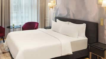 Una habitación de hotel con una cama grande, una mesita redonda con una planta, una silla roja y una mesita de noche con una lámpara.