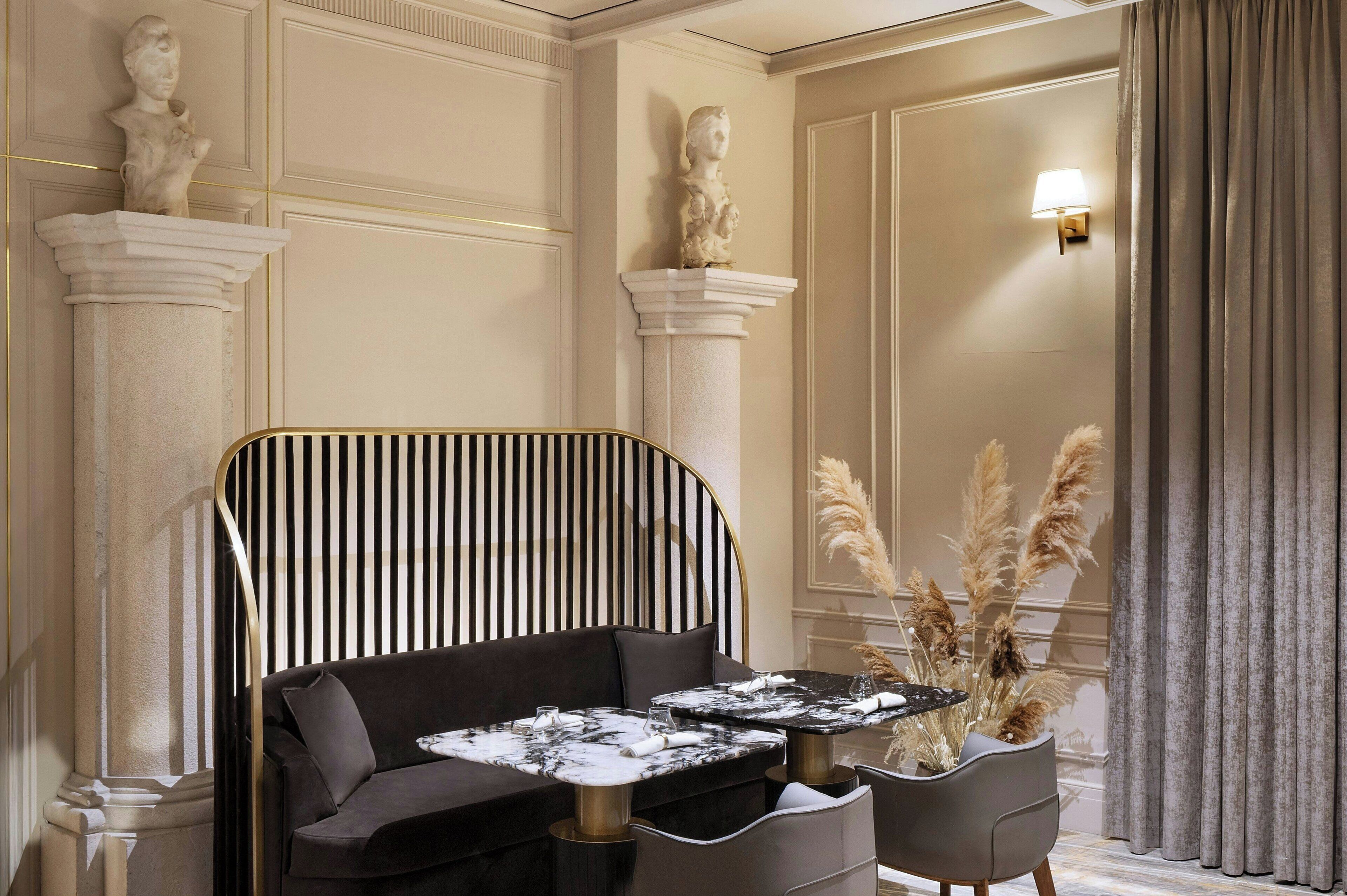 A room with a black sofa, two marble tables, and a decorative vase with pampas grass.