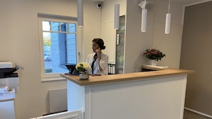 A reception desk with a white counter, a vase with flowers, and a security camera on the wall. - Signature East Hotel Falk (Hamburg)