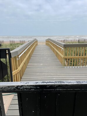 Une promenade en bois menant à une plage, avec une clôture et des zones herbeuses.