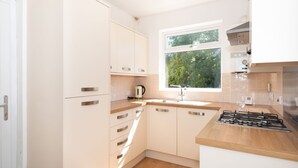Een moderne keuken met witte kasten, een houten aanrecht, een raam met uitzicht op groen, en een gasfornuis.