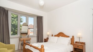 Een slaapkamer met een houten bed, een bureau, een stoel en een nachtkastje met lampen.