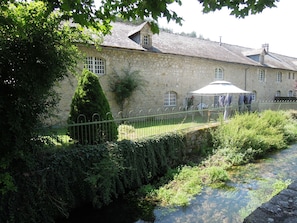 A stone building with a tiled roof, a small garden, and a water channel.