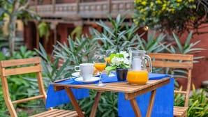 Ein Holztisch mit einer blauen Tischdecke, einer weißen Tasse, einem Glas, einer Karaffe Orangensaft und einem kleinen Topfpflanzen.