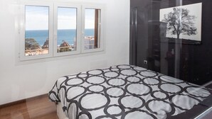 Ein Schlafzimmer mit Bett, einem Fenster mit Meerblick und einem gerahmten Bild an der Wand.