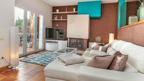 Ein modernes Wohnzimmer mit einem weißen Sofa, einem Flachbildfernseher, einem Kamin und einem Balkon mit Gartenmöbeln.