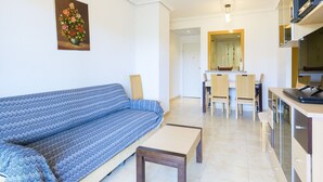 Ein modernes Wohnzimmer mit Sofa, einem Essbereich mit Stühlen und einer Küche mit Schränken und einer Mikrowelle.