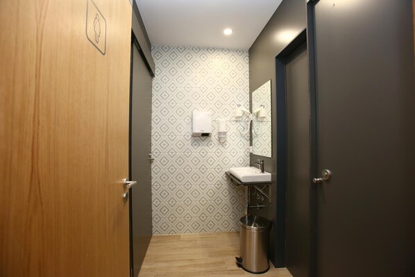 A narrow hallway with a wooden door on the left, a bathroom with a patterned wall, a sink, and a mirror. - dpaso Urban Hostel (Pontevedra)