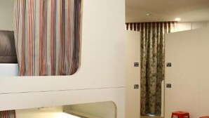 A hotel room with a striped curtain, a bed, a nightstand, and a red stool. - dpaso Urban Hostel (Pontevedra)