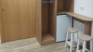 A compact room with a wooden wardrobe, a small kitchenette, and two stools. - dpaso Urban Hostel (Pontevedra)