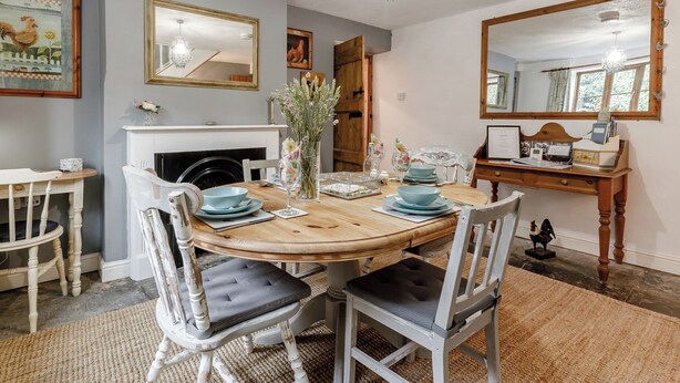 Une salle à manger avec une table ronde en bois, des chaises blanches, un lustre et une cheminée.