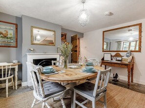 Une salle à manger avec une table ronde en bois, des chaises blanches, un lustre et une cheminée.