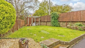 Un jardin bien entretenu, agrémenté d’une pergola en bois, d’un mur en pierre et d’un chemin de gravier.