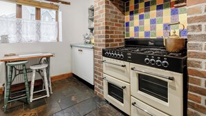 Une cuisine avec un mur en briques, un plan de travail coloré recouvert de carreaux, une cuisinière à gaz et une bouilloire.