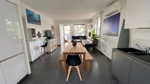 A modern kitchen with a dining area, featuring a wooden table and chairs, a built-in oven, and a large window providing natural light. - Villa Sandy Beach - Capbreton (Capbreton)