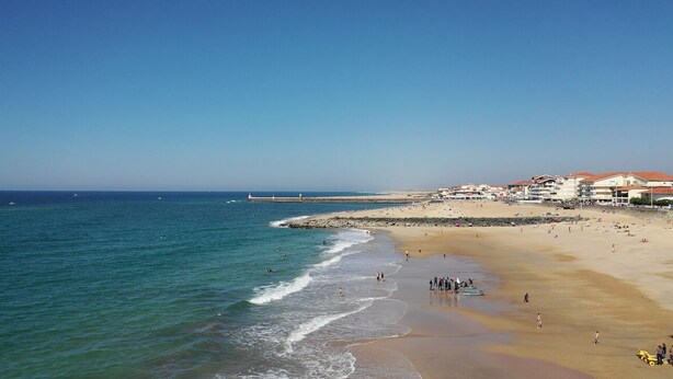 A beach with clear blue water, a sandy shore, and buildings with red roofs in the background. - Villa Sandy Beach - Capbreton (Capbreton)