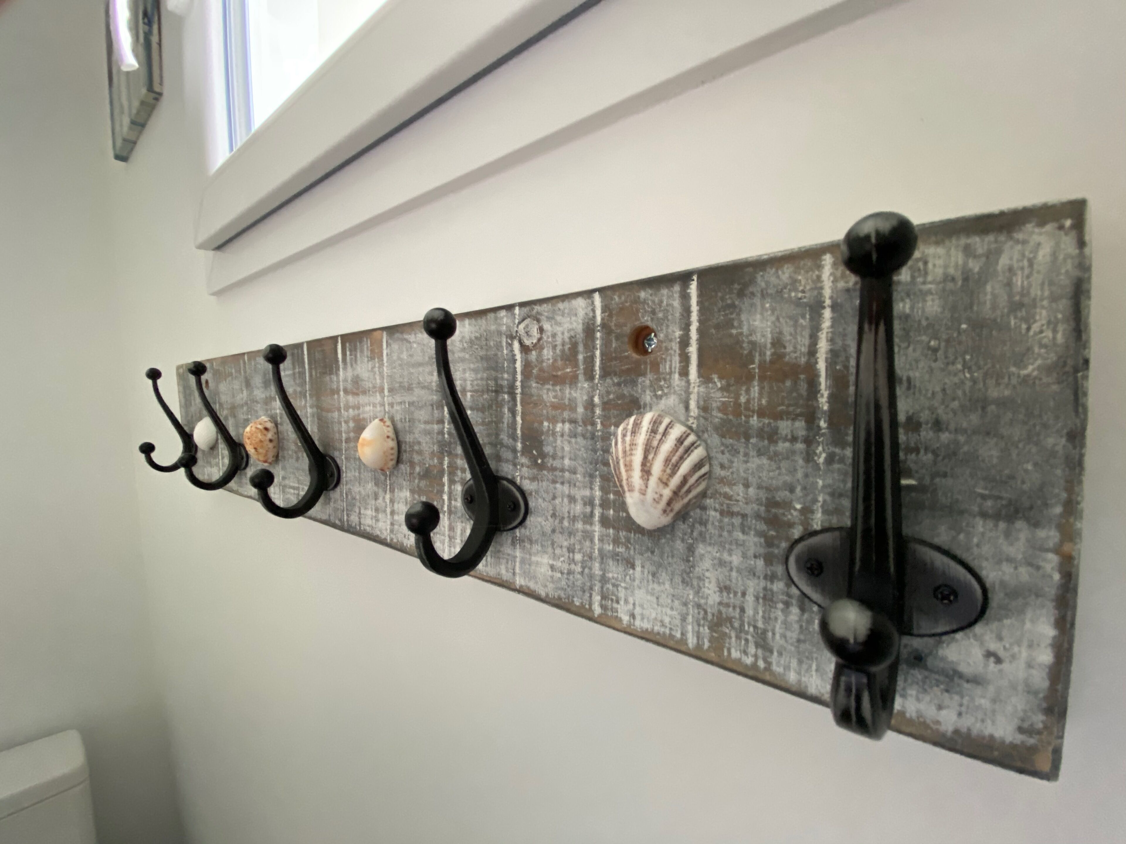 Ein rustikaler, an der Wand befestigter Garderobenständer mit fünf Haken, auf denen jeweils eine Muschel liegt.