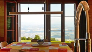A dining area with a table set for four, a bowl of fruit, and a view of a cityscape through large windows. - Stunning private villa for 6 people with WIFI, pets allowed and panoramic view (Les Cluds)