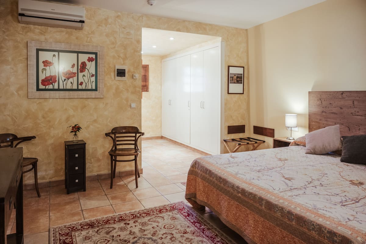 Un dormitorio con cama, escritorio, silla, armario y una puerta que da a otra habitación.