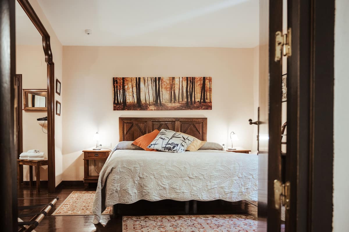 Un dormitorio con una cama grande, cabecera de madera, mesita de noche y espejo. También hay un cuadro en la pared.