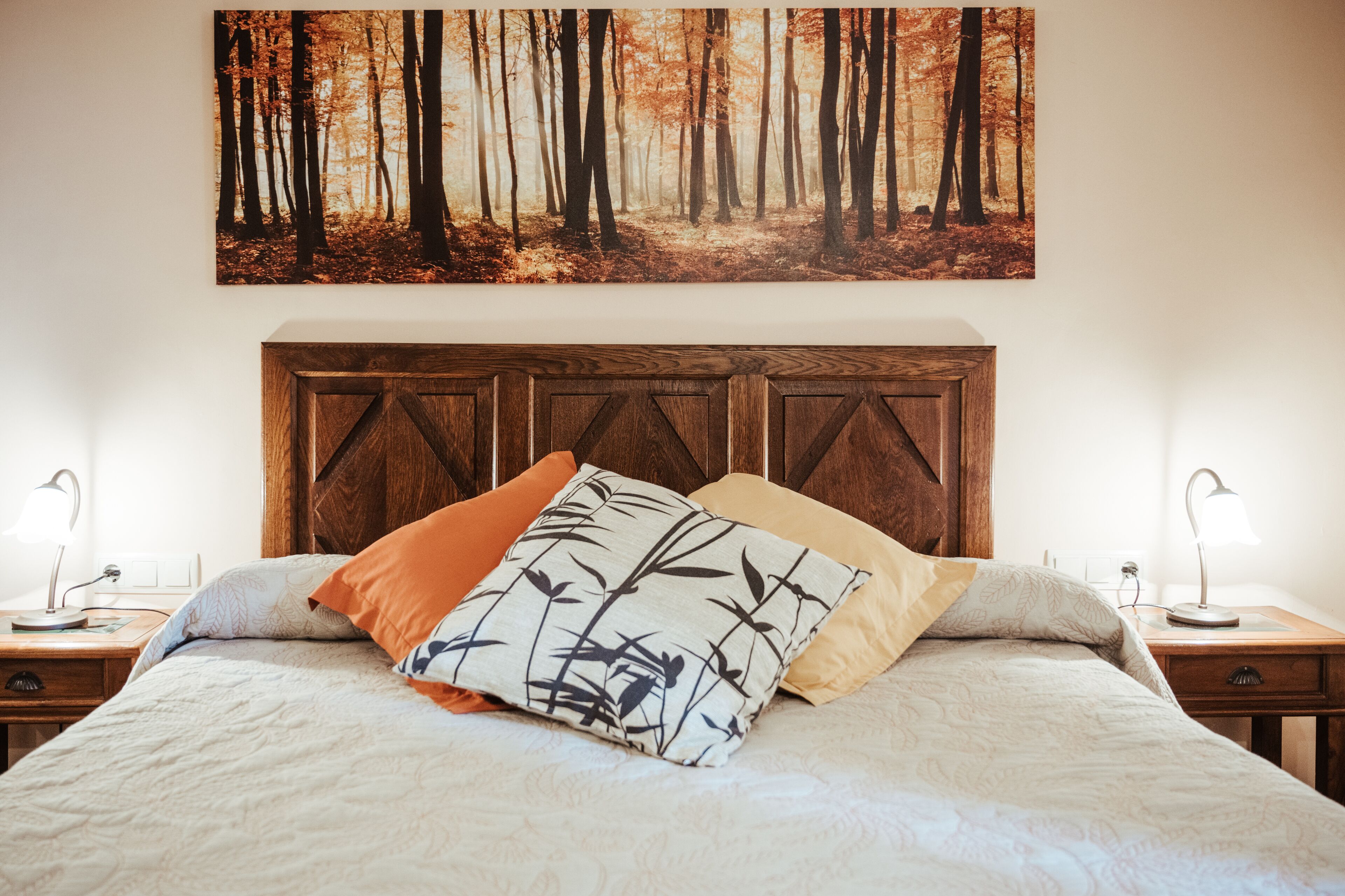 Une chambre à coucher avec un grand lit, une tête de lit en bois, deux tables de chevet avec des lampes et une décoration murale sur le thème de la forêt.