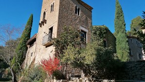 Una torre de pedra amb un balcó, envoltada d'arbres i una paret de pedra.