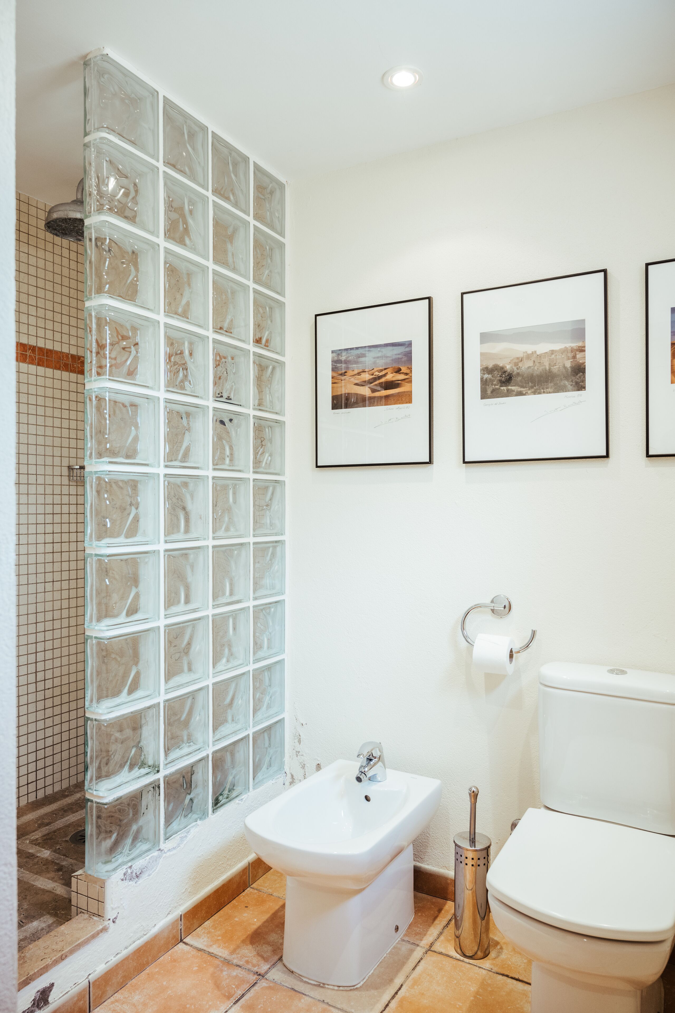 Een badkamer met een douchecabine van glas, een bidet, een toilet en ingelijste foto's aan de muur.