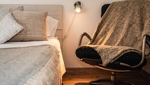 Een slaapkamer met een bed, kussens, een stoel en een wandlamp.