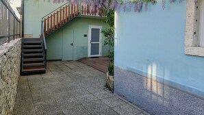 Een gebouw met een trap die naar een balkon leidt, een deur en een muur met hangende wijnranken.