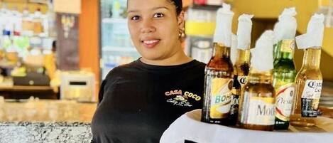 A person holding a tray with bottles of beverages in a restaurant setting.