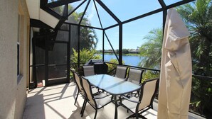 Eine Terrassengruppe im Freien mit Glastisch und -stühlen, einem Grill und Blick auf einen See.