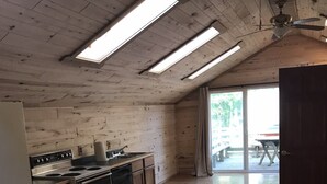 Eine Küche mit Holzausstattung, einem Herd und einem Kühlschrank. Ein Deckenventilator und Dachfenster sind vorhanden.