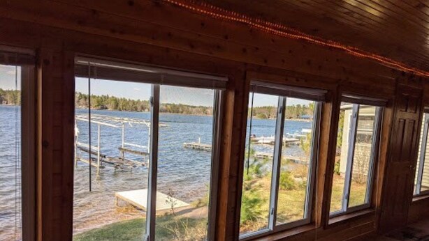 Ein Zimmer mit großen Fenstern und Blick auf einen See, Holzwände und einer Decke mit Lichterketten.