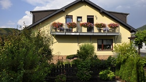 A two-story house with a balcony, surrounded by greenery and hills. - Gästehaus Panorama (Bruttig-Fankel)