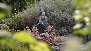 A garden statue of a figure in a hat sitting on a rock surrounded by dense shrubbery. - Gästehaus Panorama (Bruttig-Fankel)