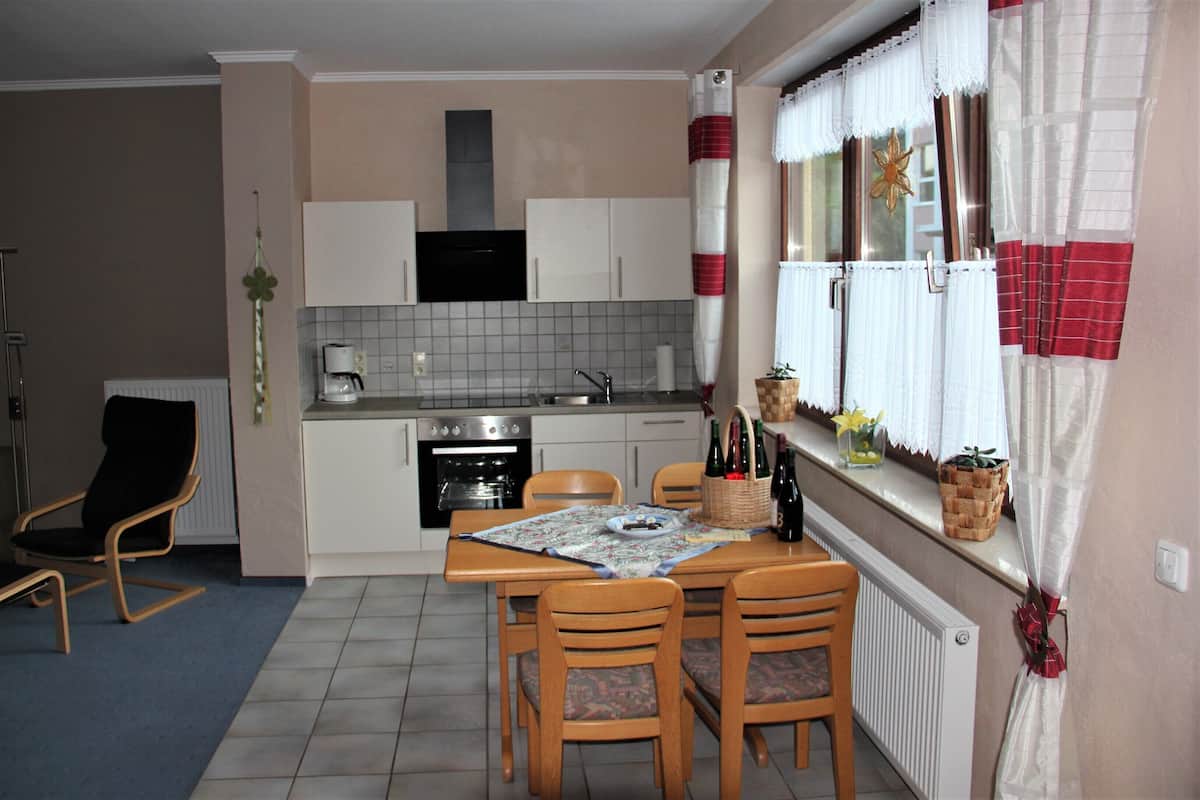 Cocina compacta con armarios blancos, horno integrado y zona de comedor con mesa y sillas.