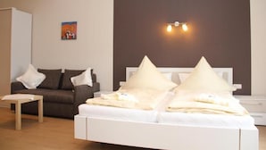 A bedroom with a white bed, two pillows, a brown sofa, a small table, and a painting on the wall. - Gästehaus Panorama (Bruttig-Fankel)