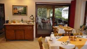 A dining area with a wooden buffet, a painting on the wall, and a view of the outside. - Gästehaus Panorama (Bruttig-Fankel)