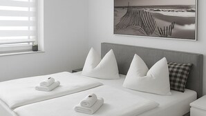 A modern bedroom with a grey bed, white pillows, and a black and white artwork above the bed.