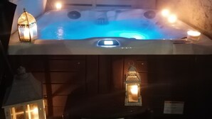 A hot tub with a wooden deck, two lit lanterns, and a white fence in the background. - Country cottage Le Mas with jacuzzi (Brassac)