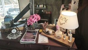 A wooden desk with a mirror, a lamp, a clock, a vase with flowers, and various items including a newspaper, a bottle, and a small plate with decorative items. - Country cottage Le Mas with jacuzzi (Brassac)