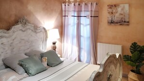 A bedroom with a bed, curtains, a lamp, a painting, and a potted plant. - Country cottage Le Mas with jacuzzi (Brassac)
