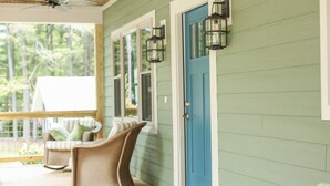 Une véranda avec des fauteuils en osier, une porte bleue et une terrasse en bois.