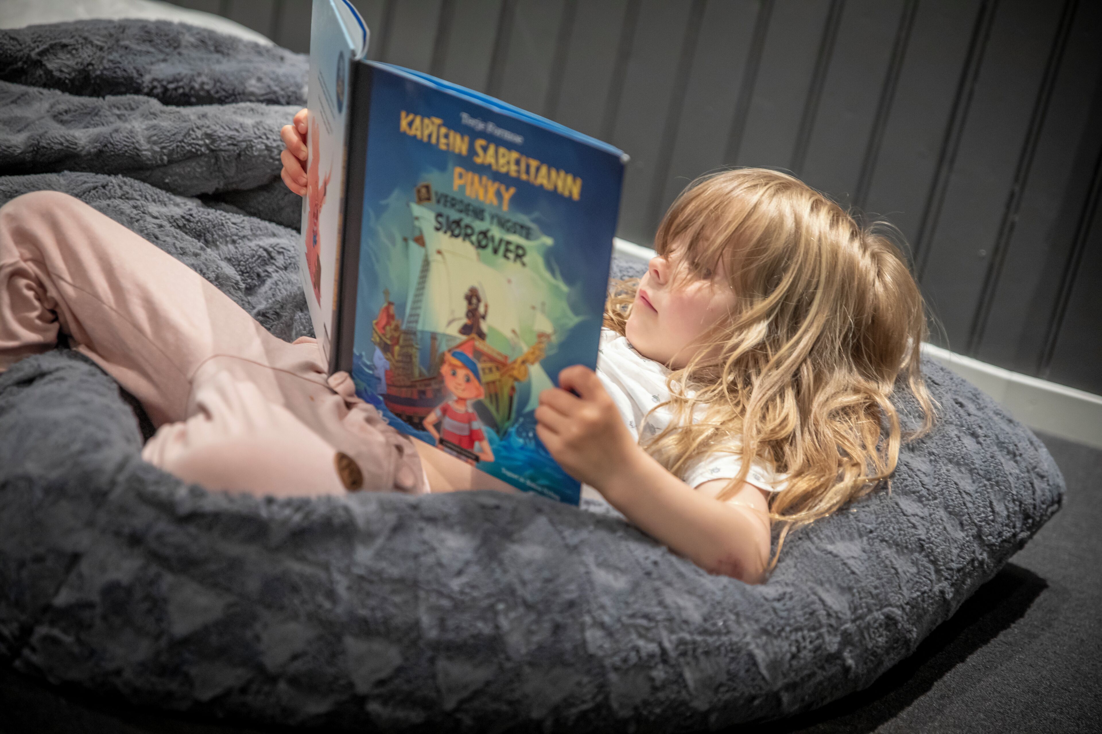 Un niño leyendo un libro sobre una cama con una manta gris.