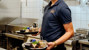 Una persona en una cocina sosteniendo una bandeja con comida.