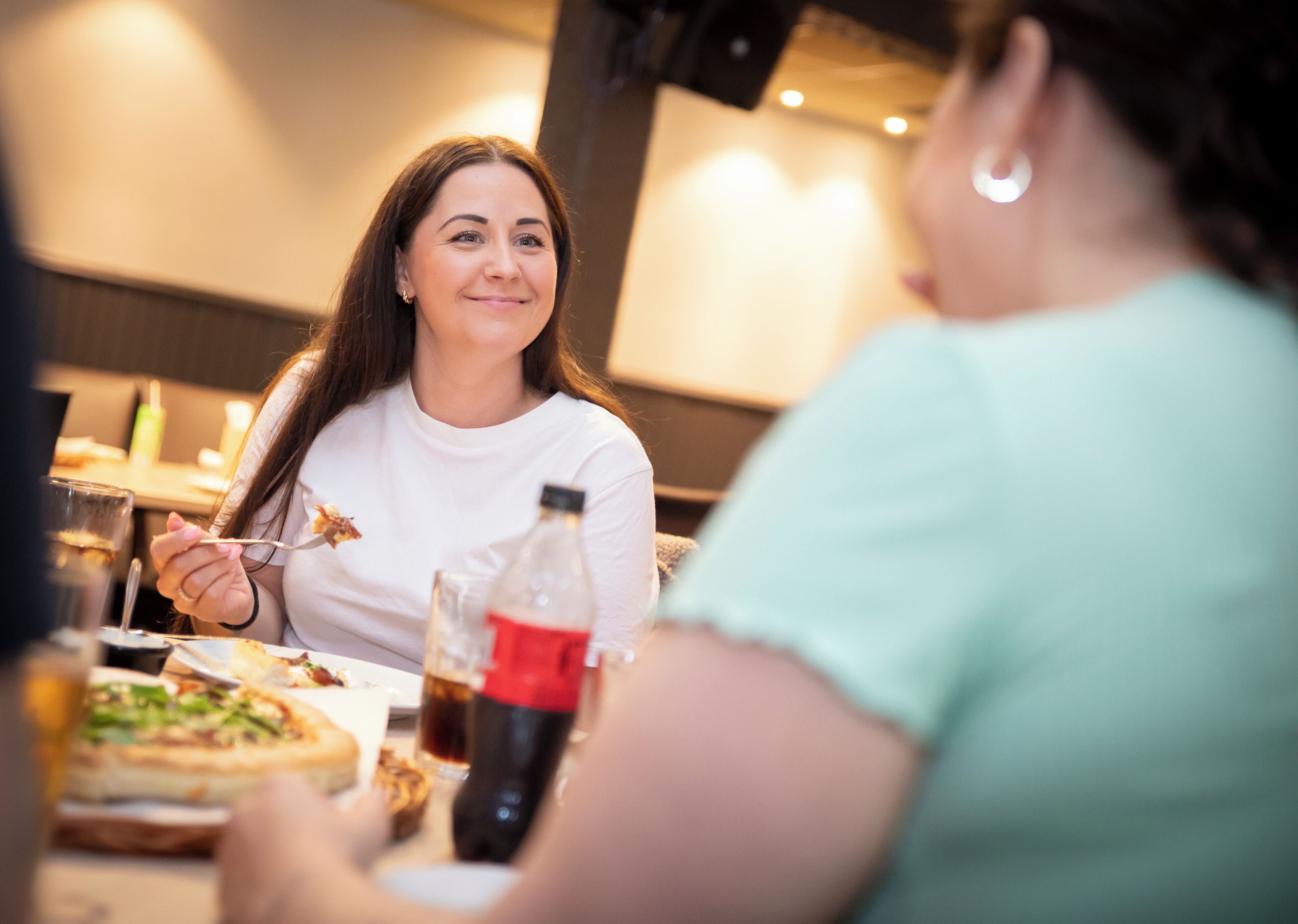 Dos personas cenando en un restaurante, con pizza y bebidas sobre la mesa.