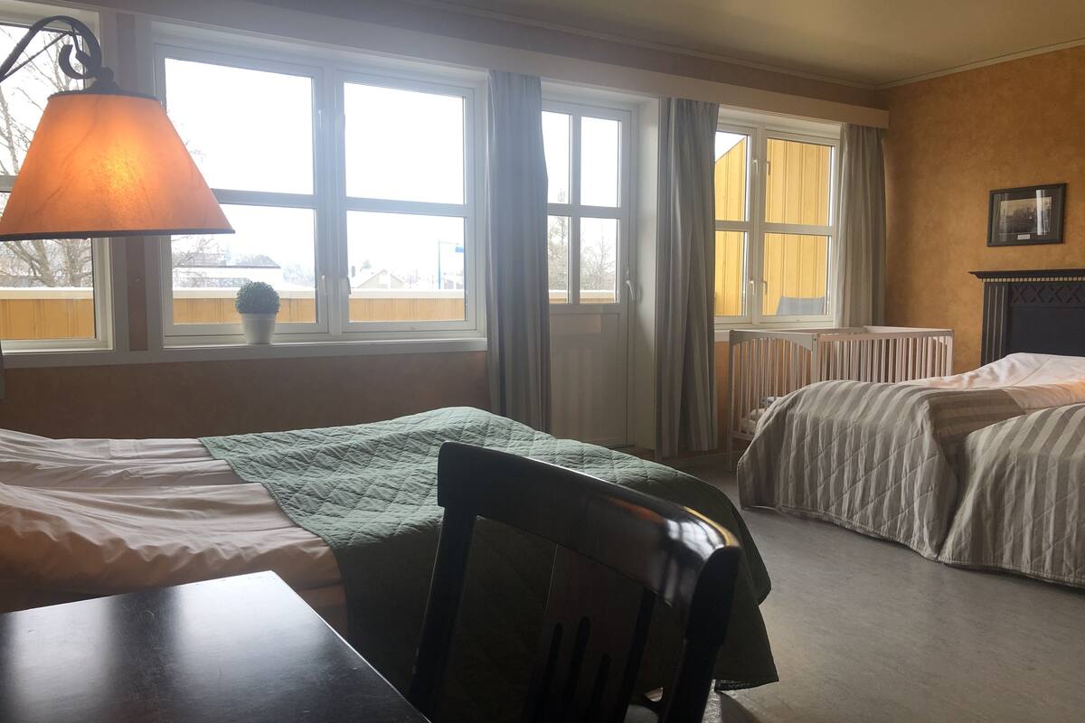 Una habitación con cama, una silla, una mesa y un ventanal con cortinas.