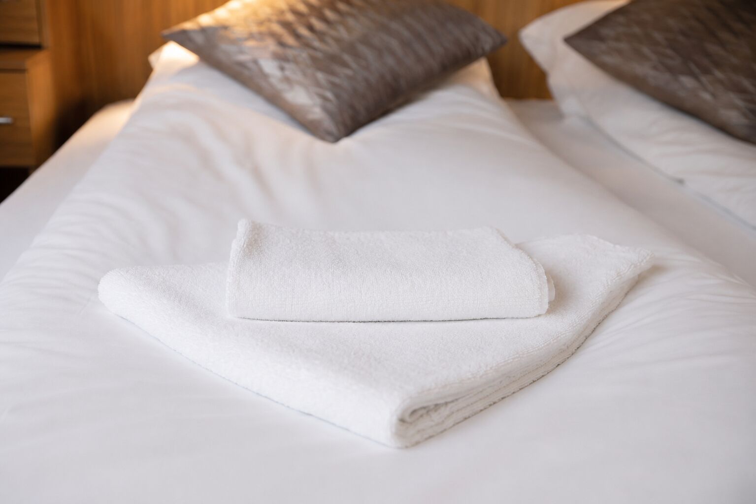 A neatly made bed with a folded white towel and two pillows.