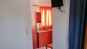 Ein Hotelzimmer mit einem Bett, einem kleinen Tisch, einem an der Wand befestigten Fernseher und einer durchgehenden Tür erkennbaren Küchenzeile.