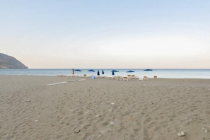 A beach with sun loungers and umbrellas, a clear sky, and a calm sea.